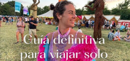 Smiling woman in a bright pink feathered festival outfit at an outdoor fair, with large white Spanish text over the image saying something about a solo travel guide.