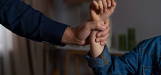 Adult hand firmly grips a child's forearm during an arm-wrestling-style grip in a home setting, suggesting guidance or restraint.