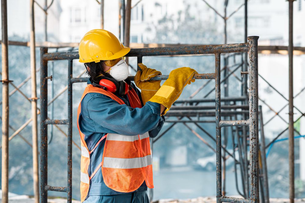 777577 - Alman | Diario-ABC.Com Construction worker in a yellow hard hat, high-visibility vest, and gloves tightening scaffolding.