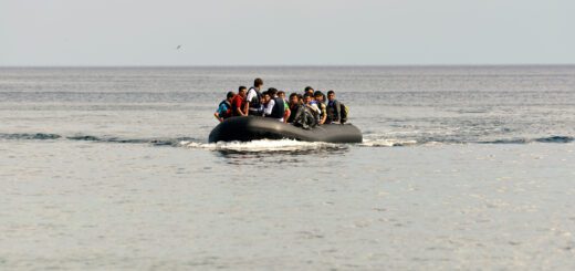 Crowded inflatable boat with passengers wearing life jackets on a calm sea near the horizon.