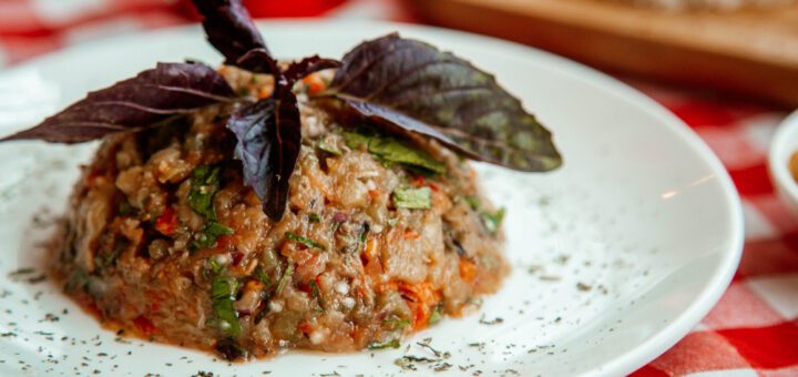 La cocina abulense encuentra nuevas formas de conquistar a vecinos y visitantes - Mounded chopped vegetable and grain salad on a white plate, garnished with purple basil leaves on a red-checked tablecloth.