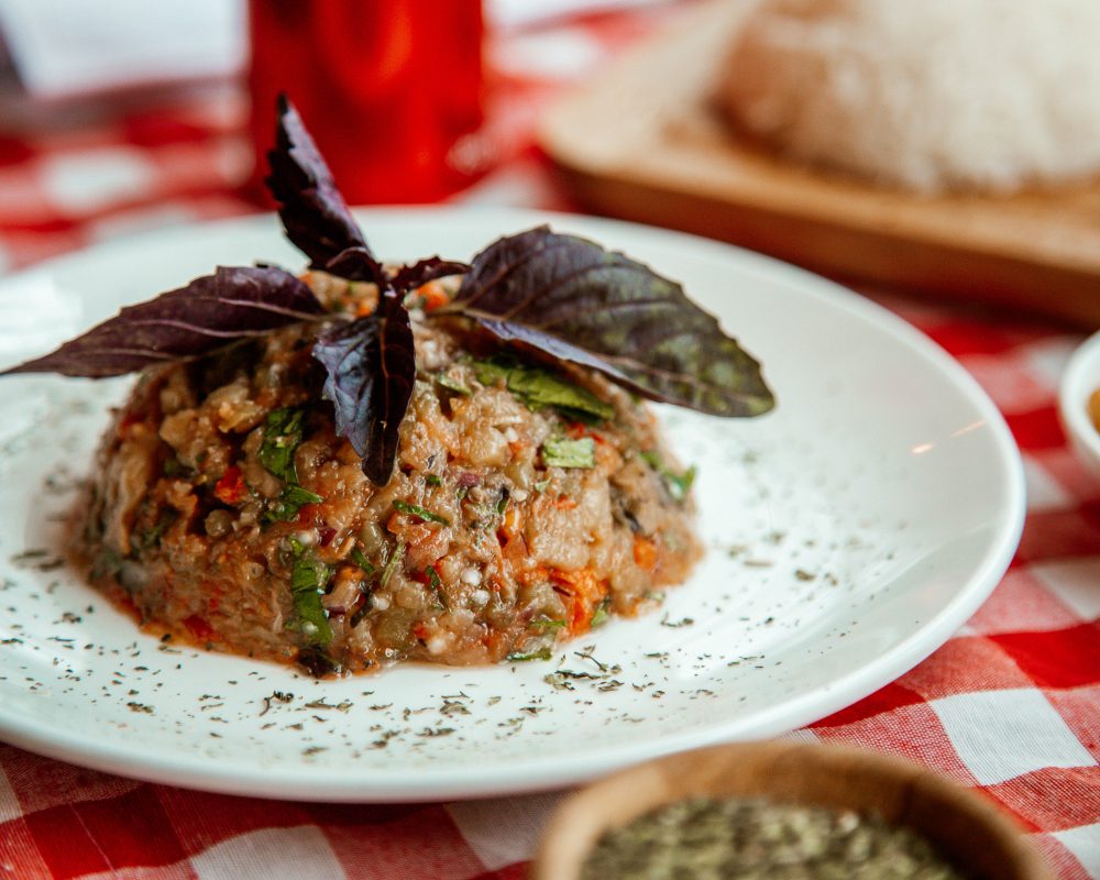 La cocina abulense encuentra nuevas formas de conquistar a vecinos y visitantes - Mounded chopped vegetable and grain salad on a white plate, garnished with purple basil leaves on a red-checked tablecloth.