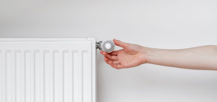 Hand adjusting a white radiator valve knob to control heat output in a room