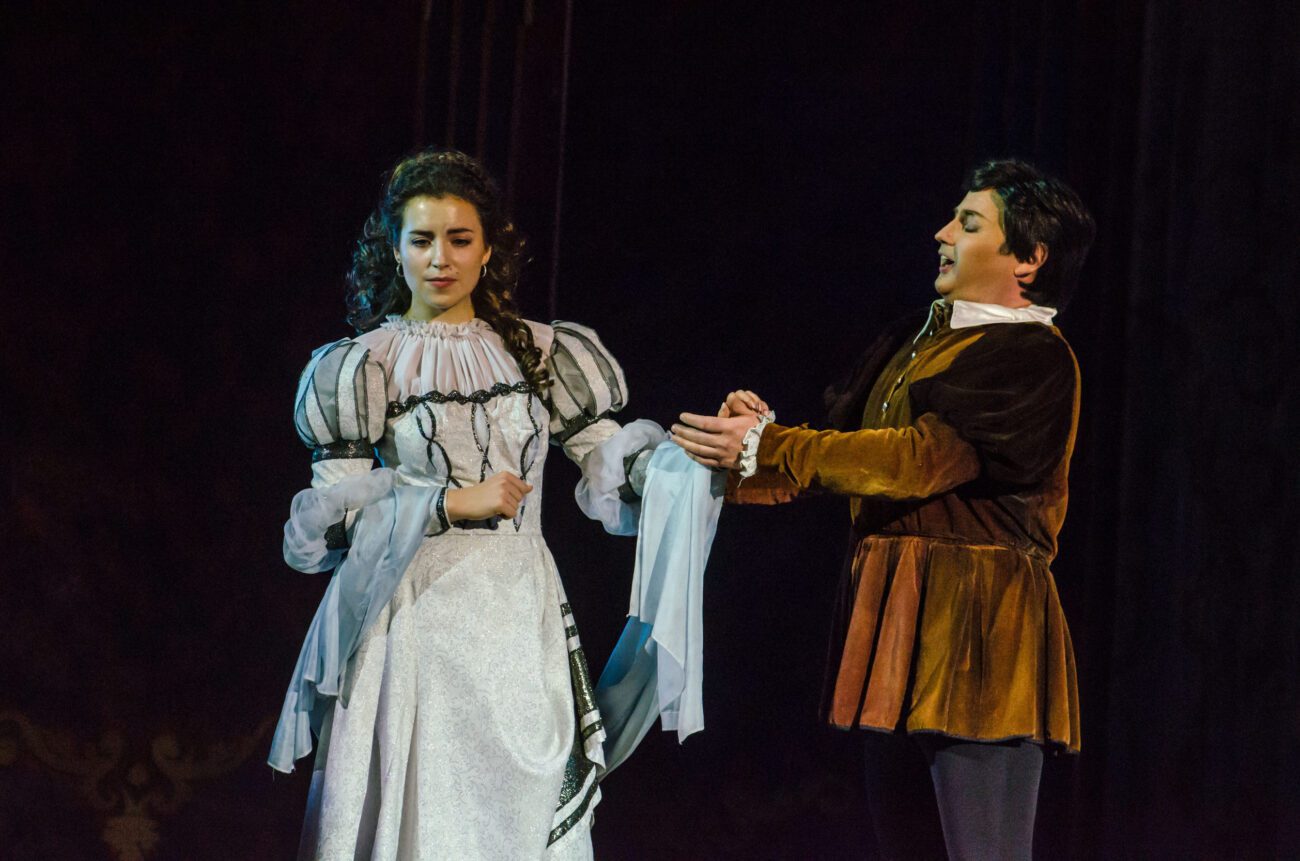 780791 Festival Opera Las Palmas | Diario-ABC.Com Stage performance: a woman in a white, ornate period dress and a man in a brown velvet tunic on stage, holding hands