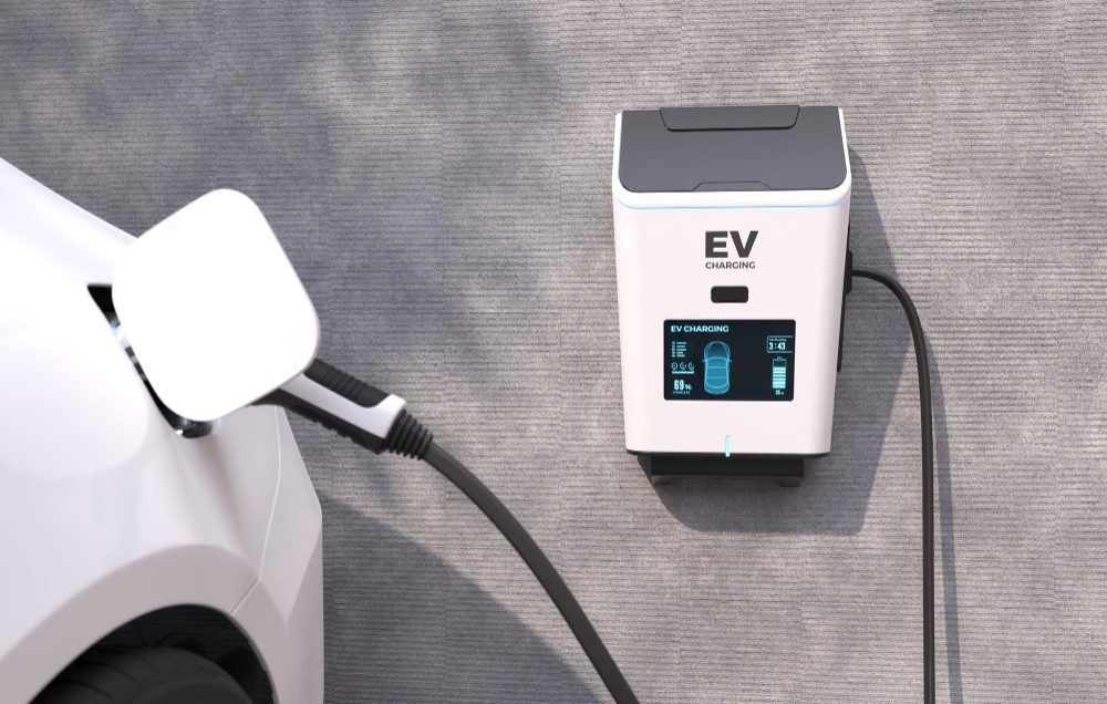 EV charging station connected to a white car, with a blue-lit display on the charger.