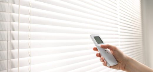 Hand holding a white remote control aimed at white horizontal window blinds