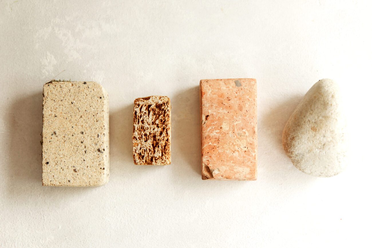782552 Travertinos y Calizas Segura | Diario-ABC.Com Four soap bars in a row: beige speckled loaf, small brown textured bar, pink rectangular soap, and a pale pebble-shaped bar on a light background.