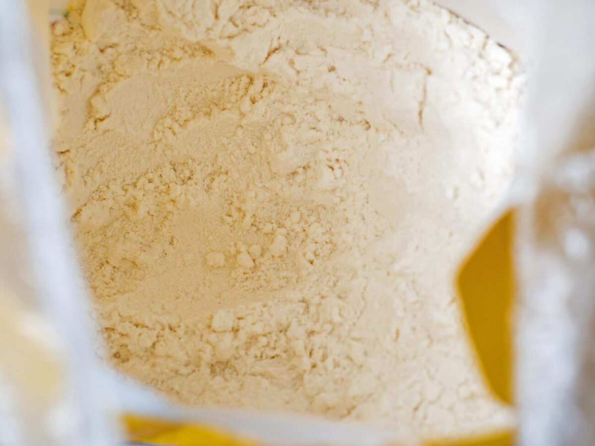 Close-up top view of a bag of white wholemeal flour | Diario-ABC.Com Close-up of fine white flour piled inside a light bag, with a yellow label visible on the side.