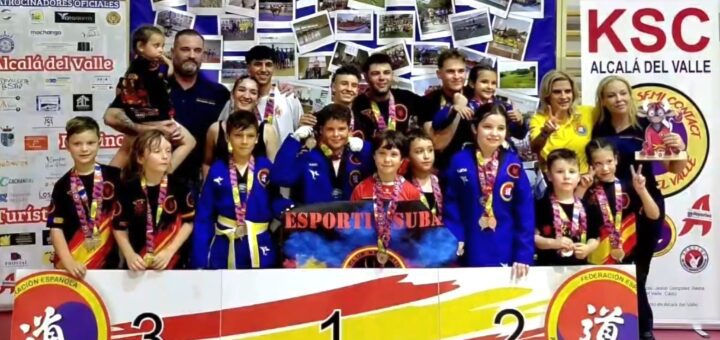 Group of children and coaches on a winners' podium with medals after a martial arts competition in Alcala del Valle.