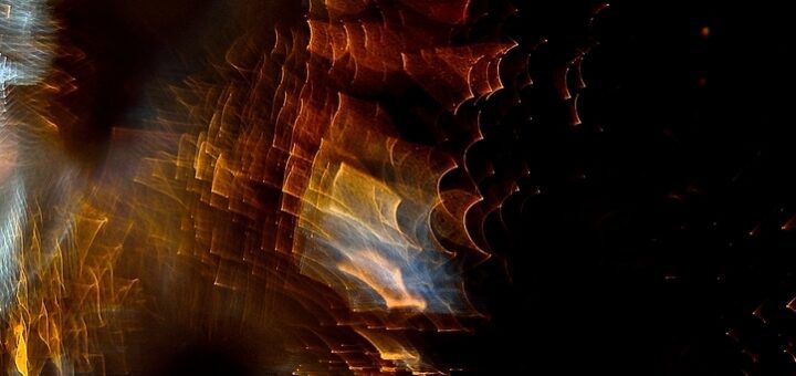 Abstract composition of blurred, colorful light orbs and streaks in orange, gold, blue on a dark background, creating a moody, dreamy pattern.
