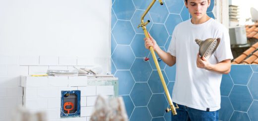 Young man installing a brass shower pipe and spray head in a bathroom under renovation.
