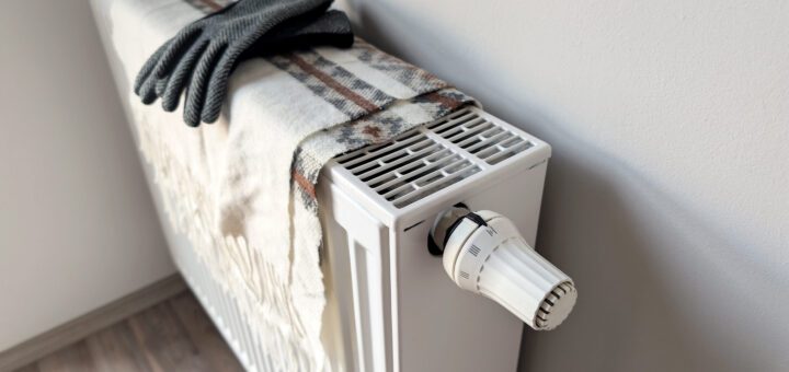 White radiator heater with a plaid scarf and gray knit gloves resting on top, in a cozy indoor setting.