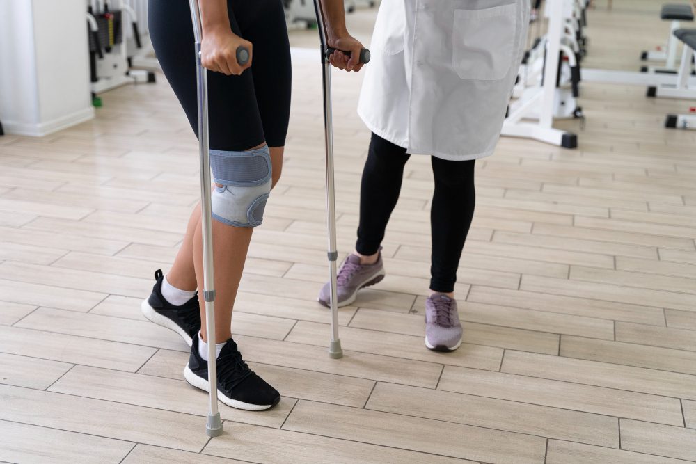 784089 - Ortopedia Neoforma | Diario-ABC.Com Person using forearm crutches and wearing a knee brace during a physical therapy session, guided by a clinician in a gym.