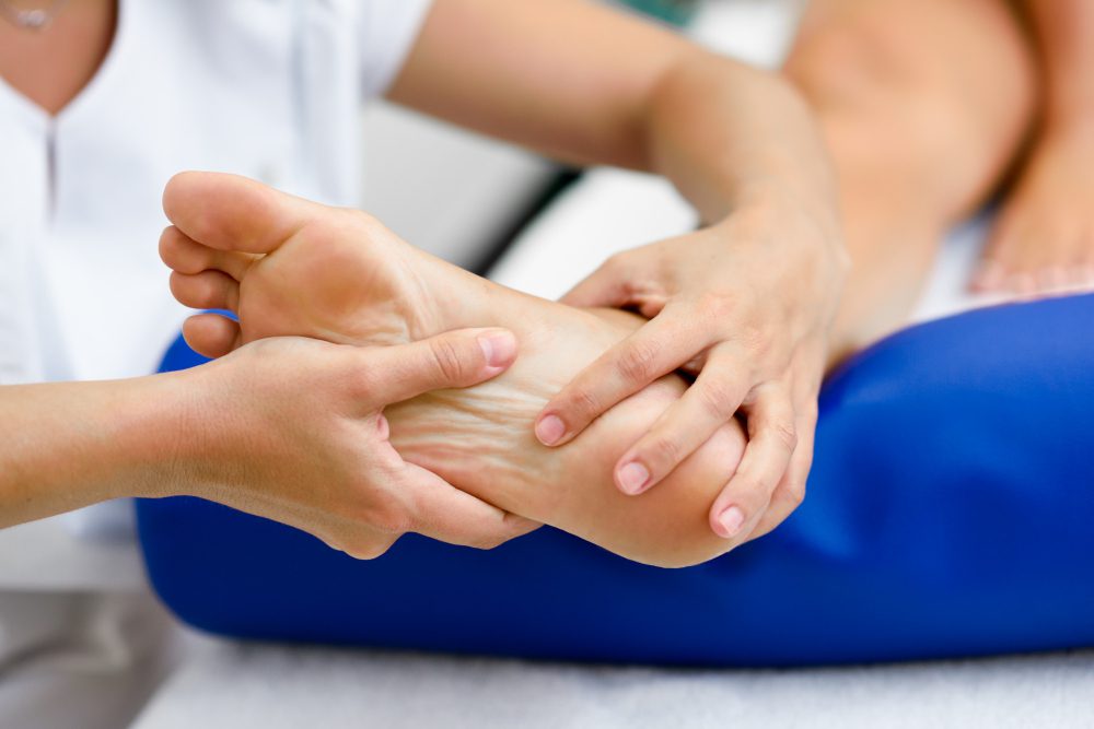 Physical therapist holds and massaging a client's bare foot during therapy session.