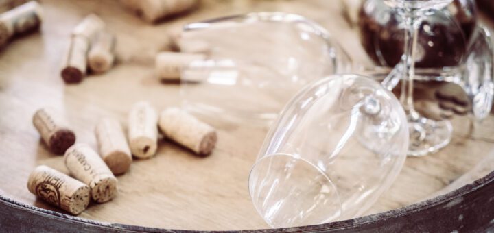 Wine corks scattered on a wooden table with a glass and decanter in the background