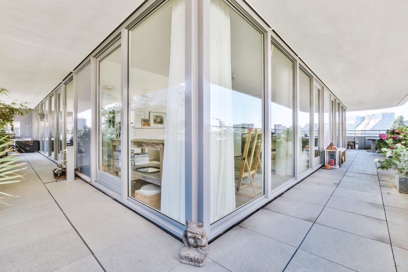 A spacious balcony of a luxury house | Diario-ABC.Com Glass-walled studio on a balcony with white curtains, visible art supplies, and easels inside; outdoor plaza and plants outside.