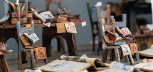 Miniature wooden chairs piled with colorful drawings and scraps, set in an art installation.