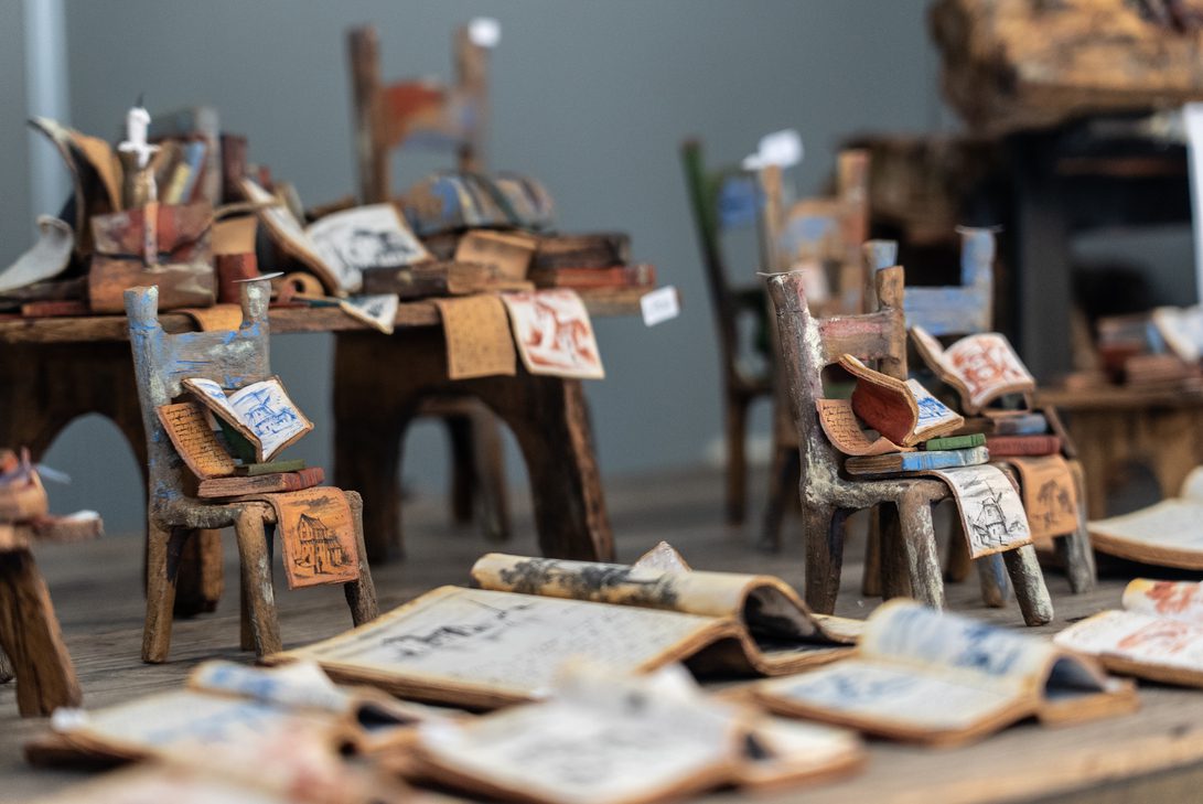 Feria artesania otoño 26 - IP | Diario-ABC.Com Miniature wooden chairs piled with colorful drawings and scraps, set in an art installation.