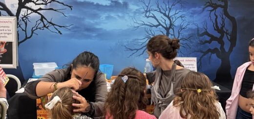 Children sit at a table getting Halloween makeup from two adults in a mall, with a blue Halloween backdrop reading 'HALLOWEEN GRAN PLAZA' behind them